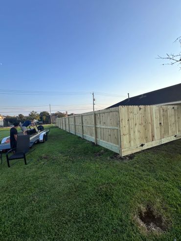 Two men near a newly installed wooden fence on a sunny day.