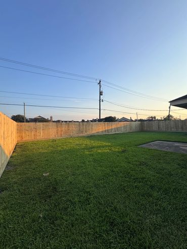 A spacious backyard with green grass and a wooden fence under a clear blue sky.