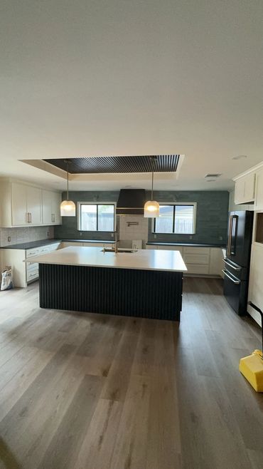 Modern kitchen with a large island, pendant lights, and black appliances.