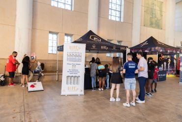 People gather at booths inside a spacious hall during an event.