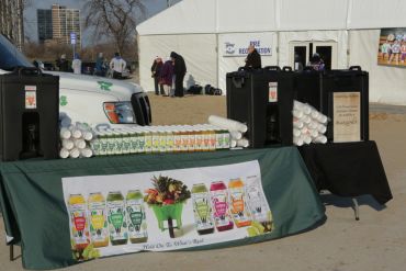 Outdoor hydration station with bottled juices and water dispensers near a registration tent.