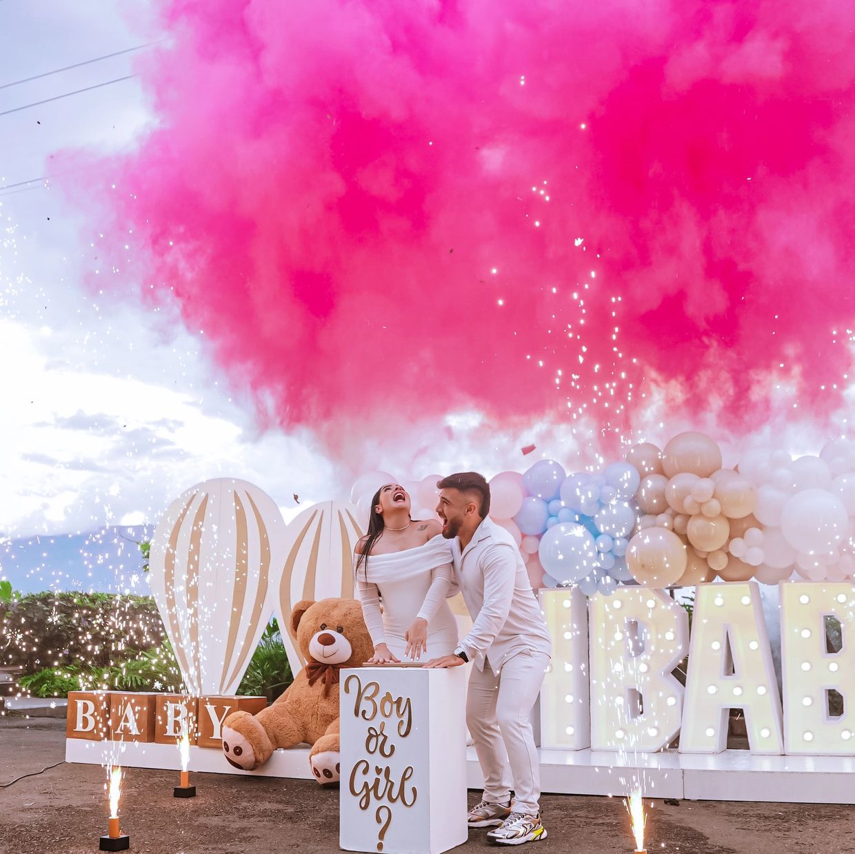 Couple celebrates gender reveal with pink smoke and balloons.