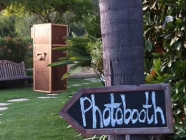 Chalkboard sign pointing to a vintage-style photobooth in a garden.