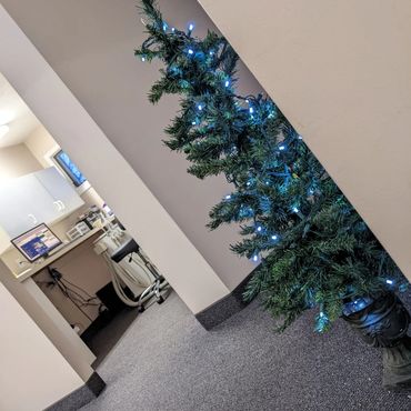 A small Christmas tree in a hallway with a dental operator in the background with a computer and cha