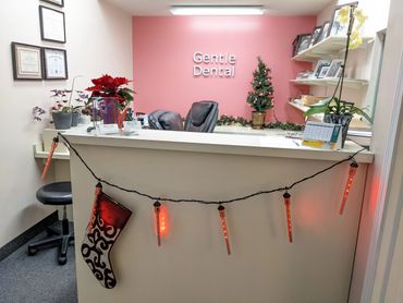 A reception desk with red icicle lights and a stocking hanging from it, there are some plants on the