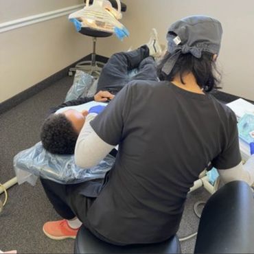 Back view of a dentist working on a patient, the dentist is wearing scrubs and the patient is laid b