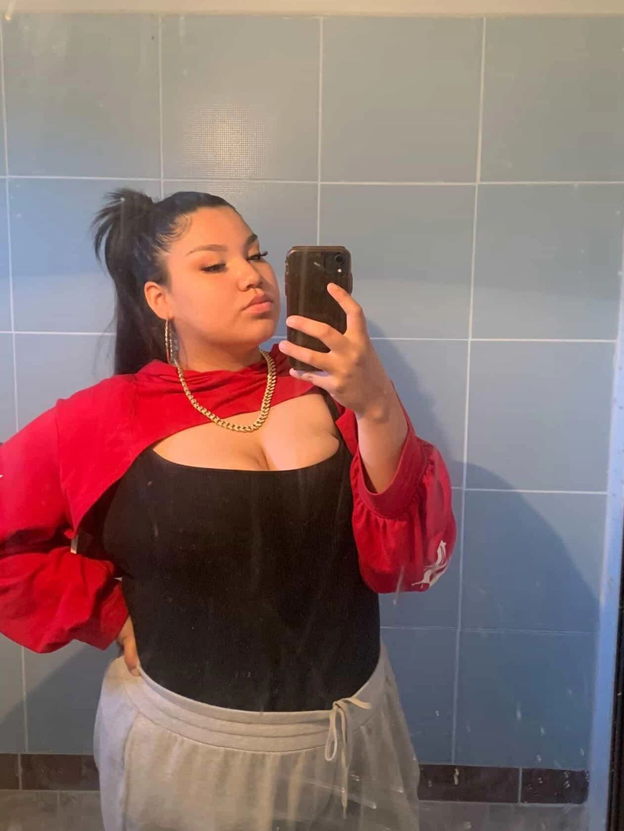 Native Woman taking a mirror selfie in casual outfit with red hoodie and gold chain.