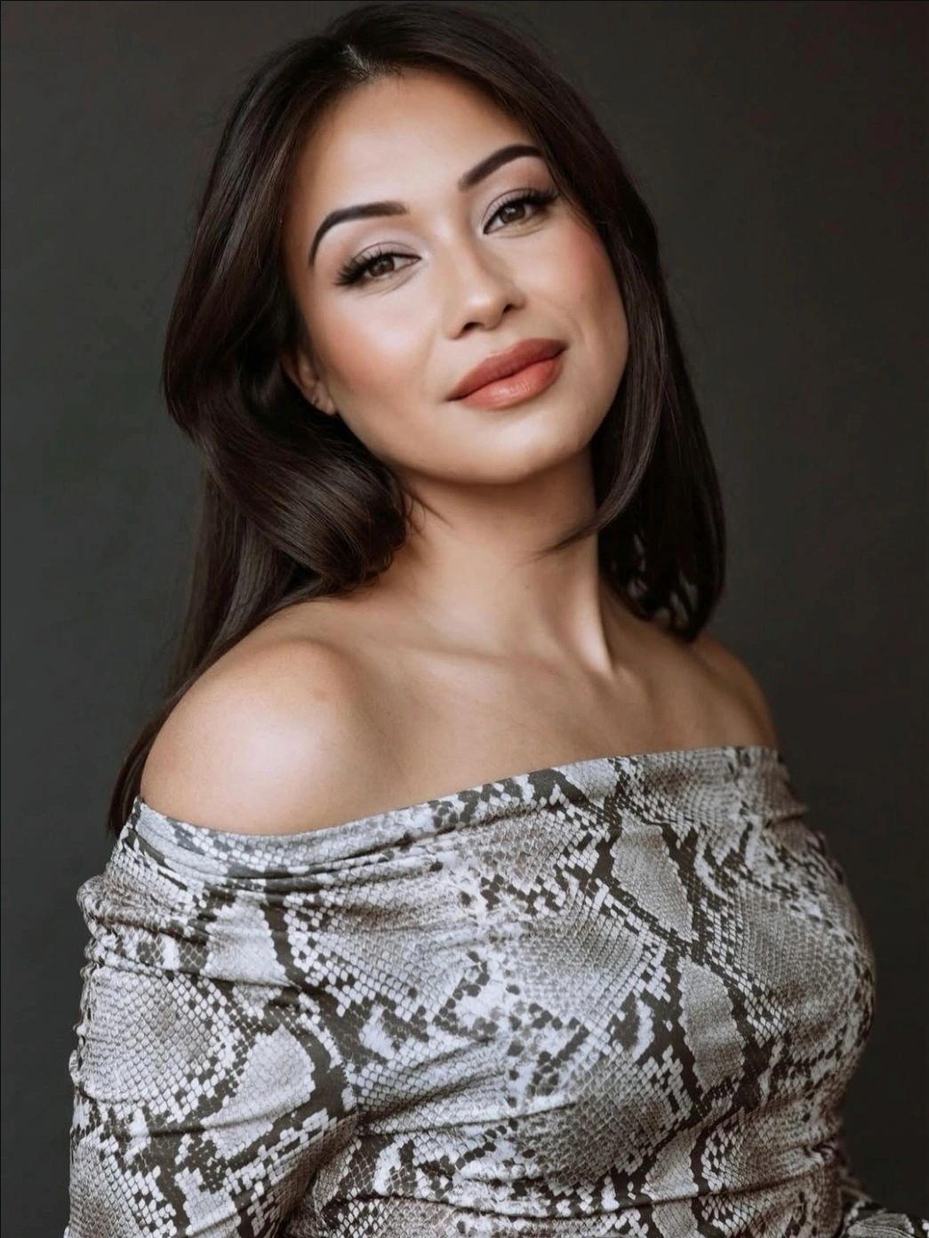 Woman with long dark hair wearing an off-shoulder snake print top.
