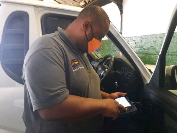 Mechanic wearing a mask using a diagnostic machine inside a car.