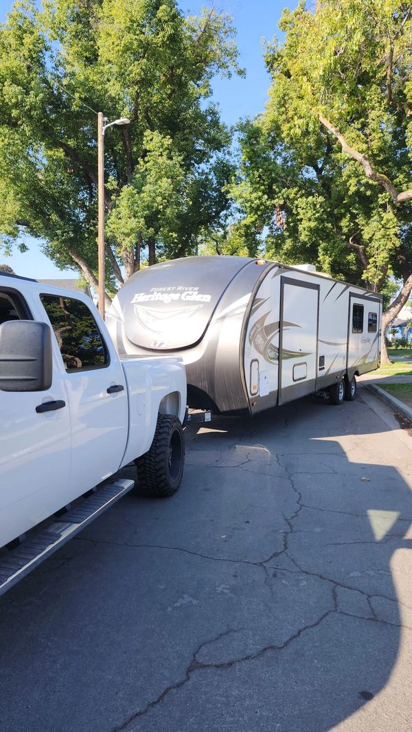 A white truck towing a Forest River Heritage Glen travel trailer on a sunny day.