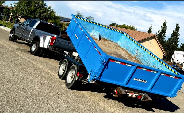 A silver pickup truck towing a large blue dump trailer on a suburban street.