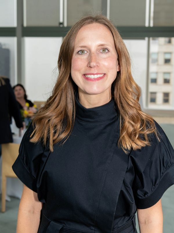 Smiling woman with wavy hair wearing a black dress indoors.