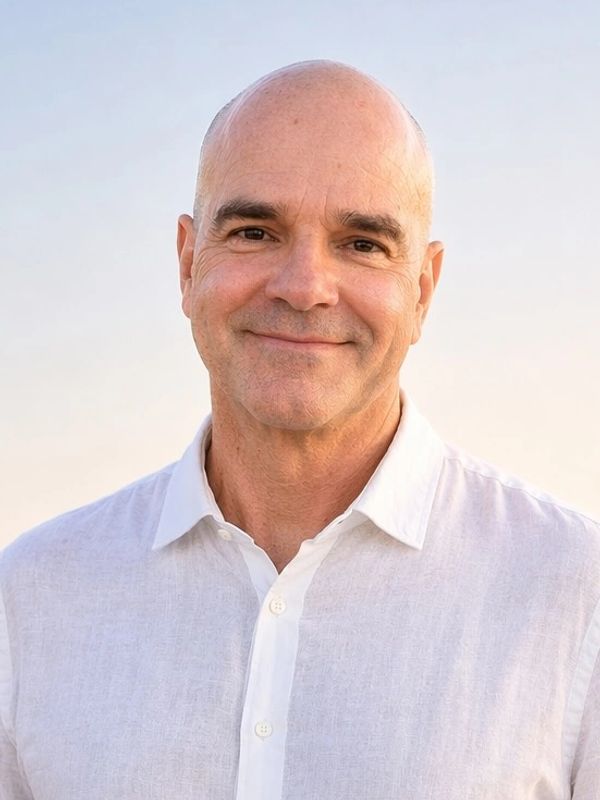 Smiling bald man in a white shirt against a clear sky background.