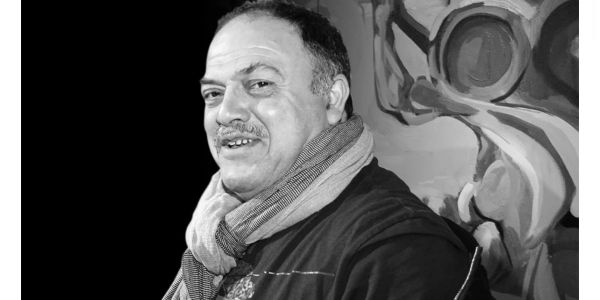Black and white portrait of a smiling man wearing a scarf.