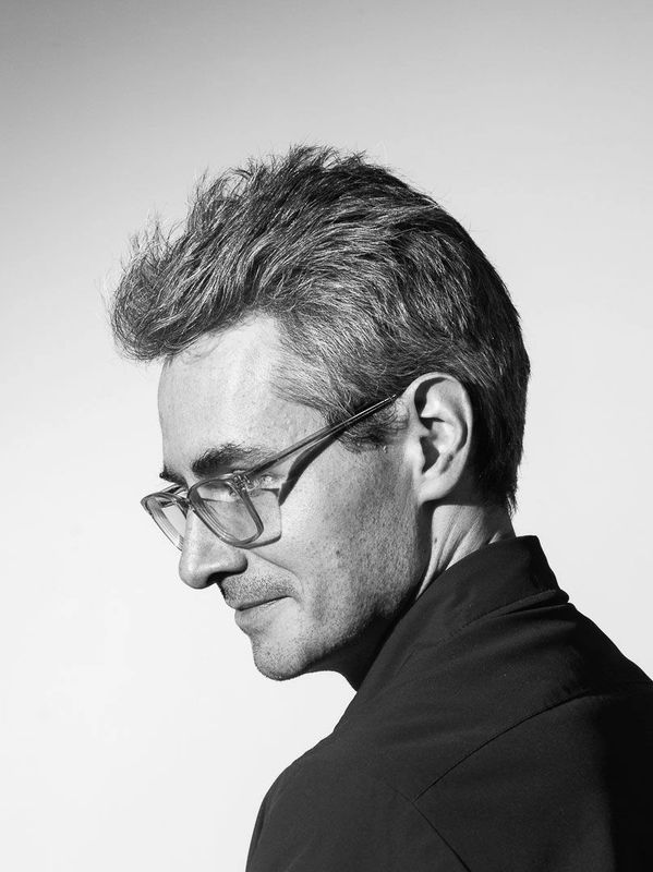 Black and white profile portrait of a man with glasses looking down thoughtfully.