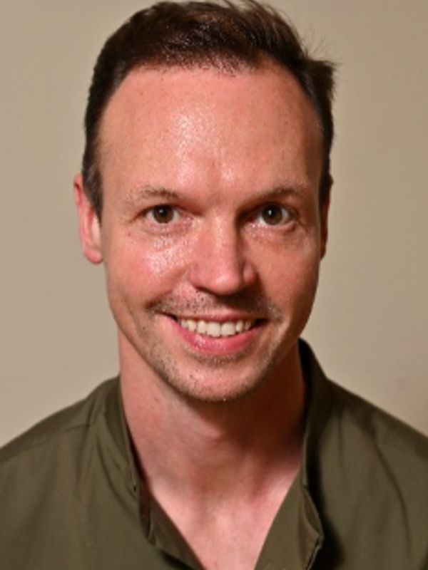 Smiling man with short hair and a green shirt.