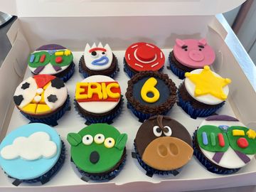 Colorful Toy Story-themed cupcakes in a box, including characters and symbols.
