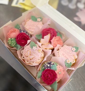 Box of beautifully decorated cupcakes with floral designs and pastel colors.