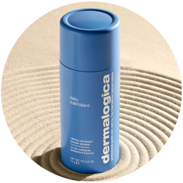 Blue Dermalogica Daily Milkfoliant bottle on textured sand.