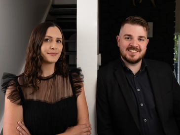 Two real estate agents standing in a home next to a wall.