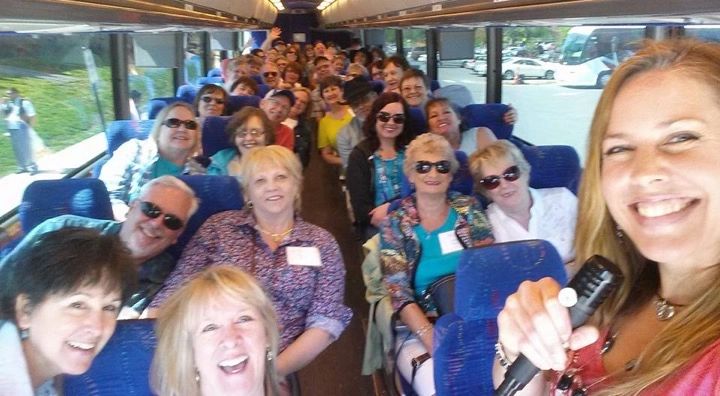 Smiling group of people on a bus, taking a selfie with a microphone.