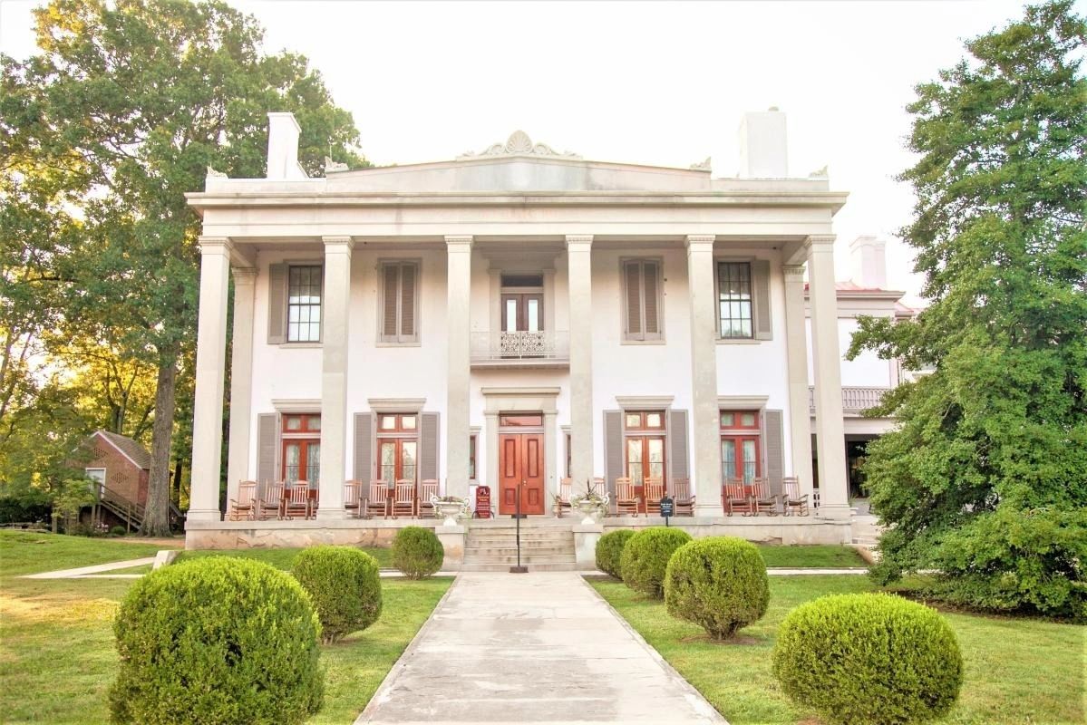 Historic mansion with tall columns and manicured bushes.