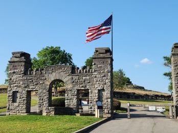 Stone gate with American flag flying above on a clear day.