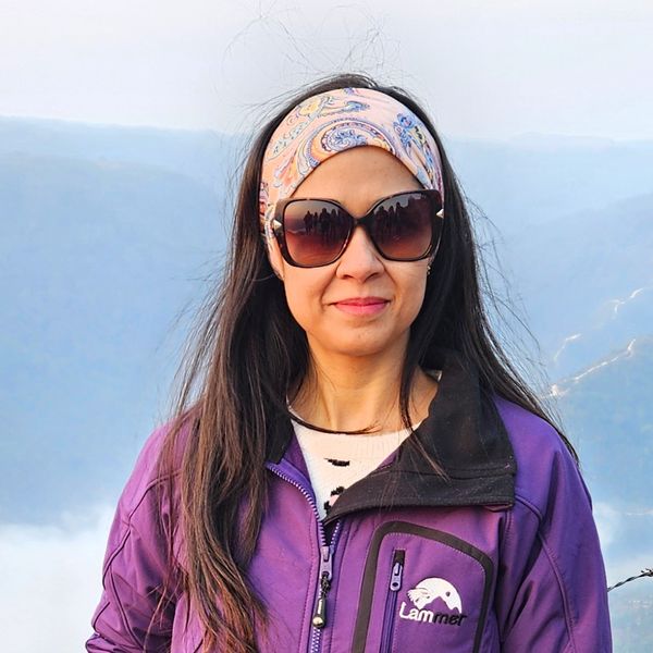 Woman in sunglasses and purple jacket with scenic mountain background.