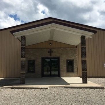 Simple church entrance with a cross above the door under a cloudy sky.