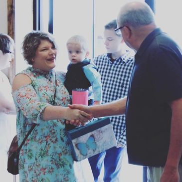 Woman holding baby shakes hands with an older man in a social setting.