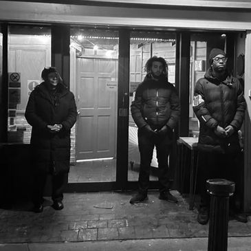 Three people standing outside a building at night, dressed warmly in coats.