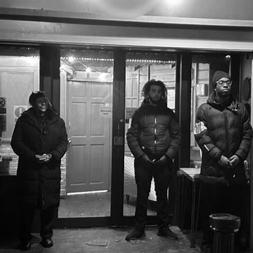 Three people standing outside a building at night, dressed warmly in coats.
