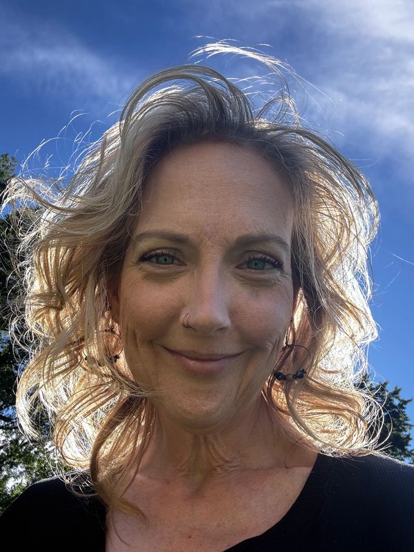Smiling woman with curly hair outdoors under blue sky.