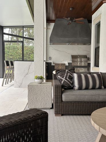 Covered outdoor living area featuring woven lounge furniture, patterned cushions, a textured accent 