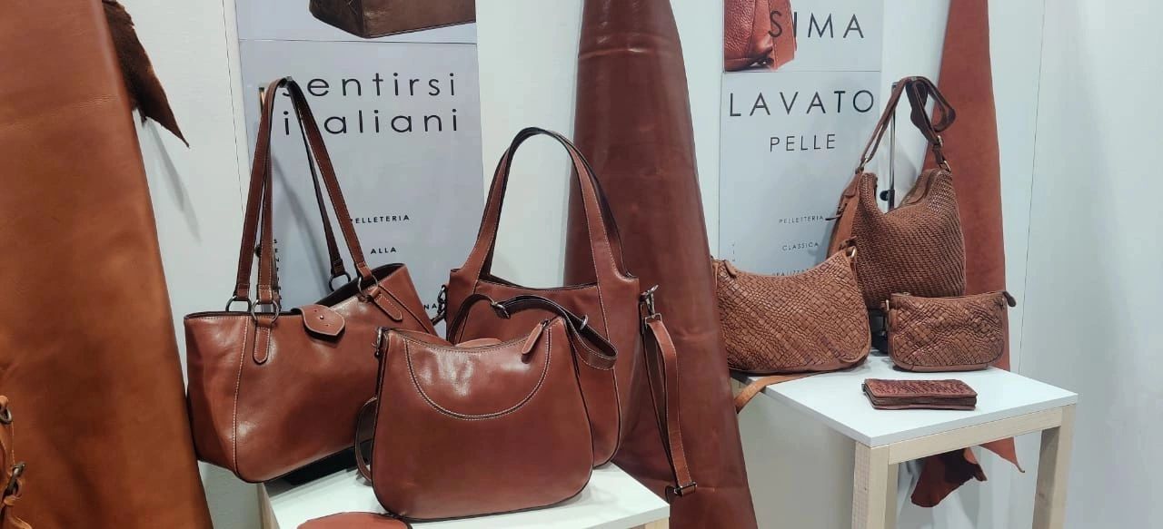 Display of stylish brown leather handbags and accessories on tables.