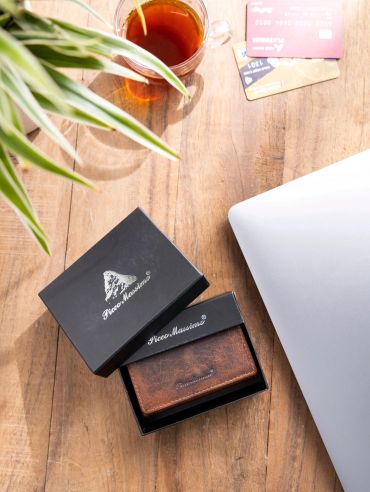 A brown leather wallet in a black box on a wooden table with a laptop and tea.