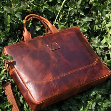 Elegant brown leather briefcase placed on green foliage.