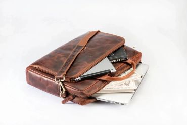 A brown leather briefcase partially open with books and a laptop inside.