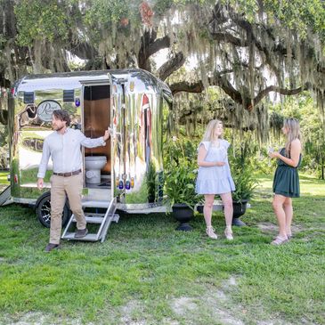 Vintage silver restroom trailer under a tree with three people