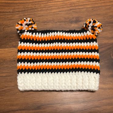 Crocheted hat with orange, black, and white stripes and pom-poms.