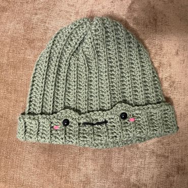 Crocheted green beanie with a cute face.