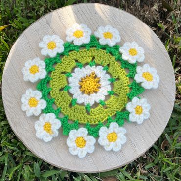 Crocheted floral mandala with daisies on a wooden board.