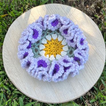 Crocheted floral piece with ruffled purple edges on wooden plate.