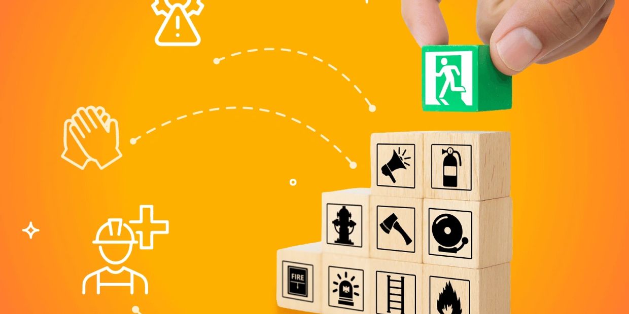 Hand stacking safety icon blocks with emergency exit symbol on top.