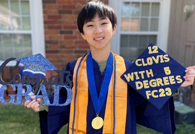Graduating student in cap and gown holding celebratory signs outdoors.
