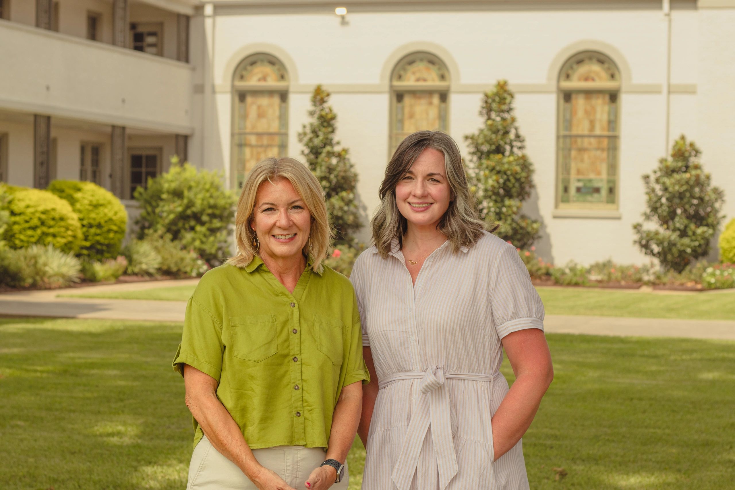 Two smiling women standing outdoors in front of a building.