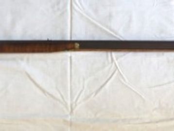 A vintage long rifle with a wooden stock and metal barrel on a white cloth.