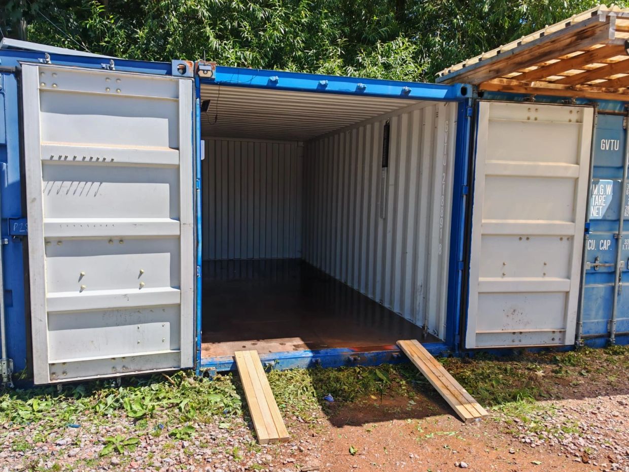 Empty shipping container with open doors and wooden ramps.