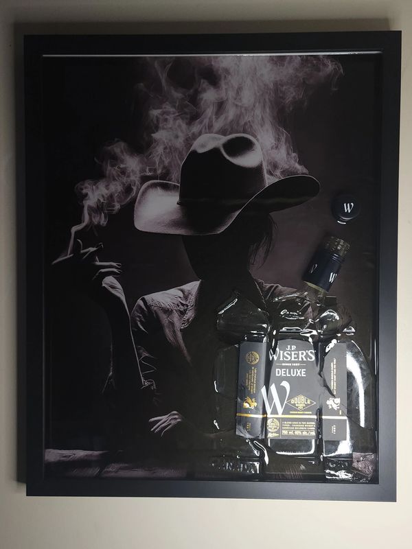 Silhouette of a person with a hat smoking, with a whiskey bottle.