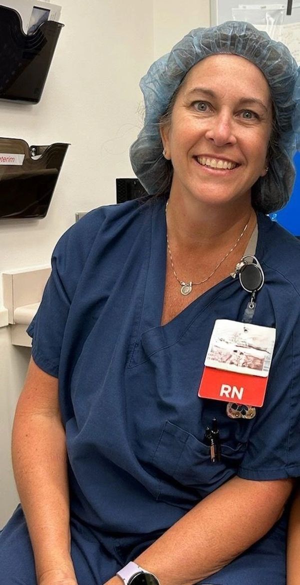 Smiling registered nurse in blue scrubs and hairnet.